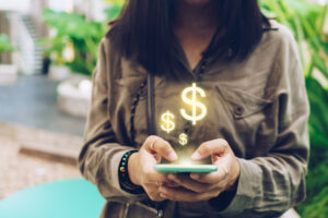 woman using phone with money signs floating above